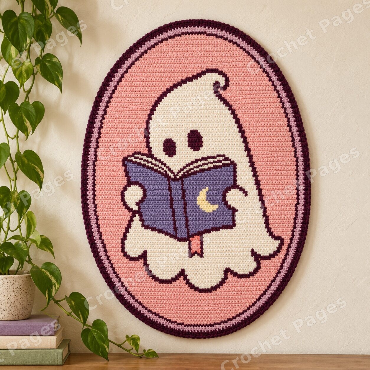 Mockup of an oval crochet wall hanging with an ivory reading ghost, purple crescent-moon book, pink background and curved dark plum edge.