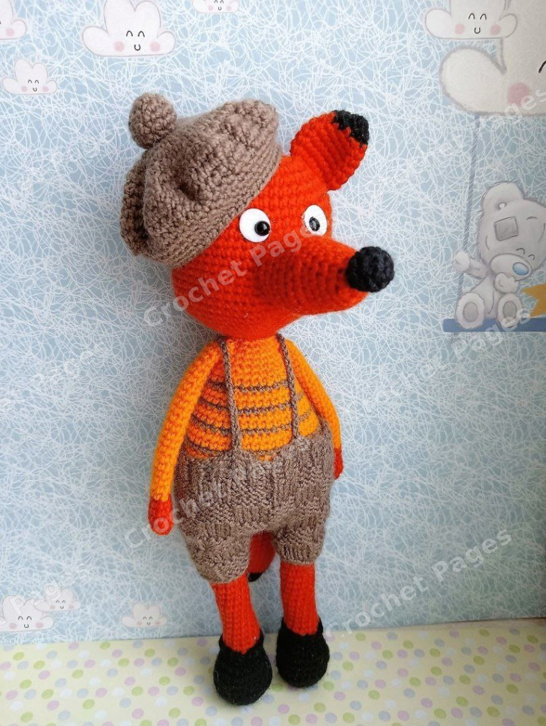 Orange crocheted fox with a brown beret, striped body and knitted suspender shorts.