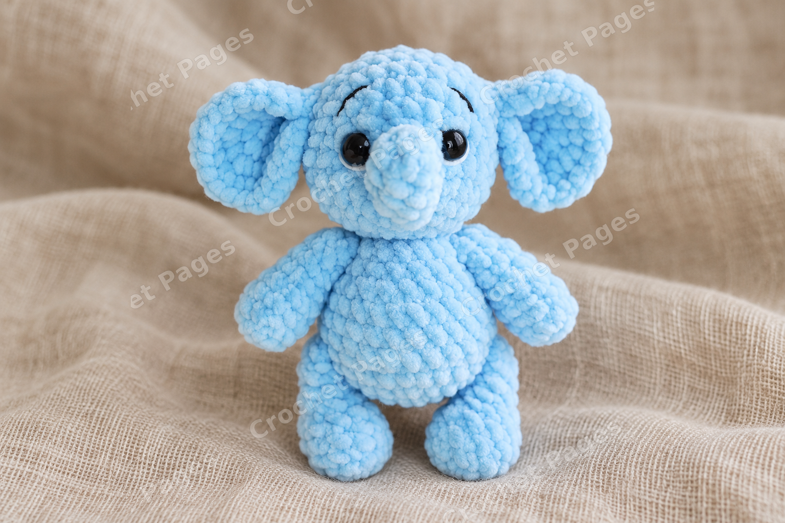 Small blue plush crochet elephant with large ears and a curled trunk; another view of the finished crochet sample.