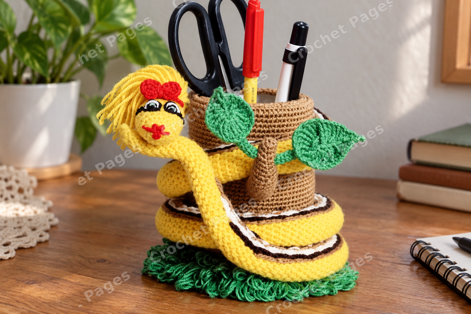 Crocheted snake coiled around a tree shaped pencil holder with leaves; another view of the finished crochet sample.