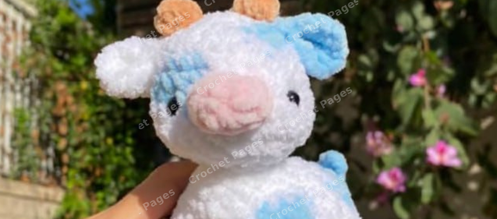 Make a four-legged cow with blue-and-white colorwork patches, tiny horns, folded ears, a pink muzzle and a short tail.