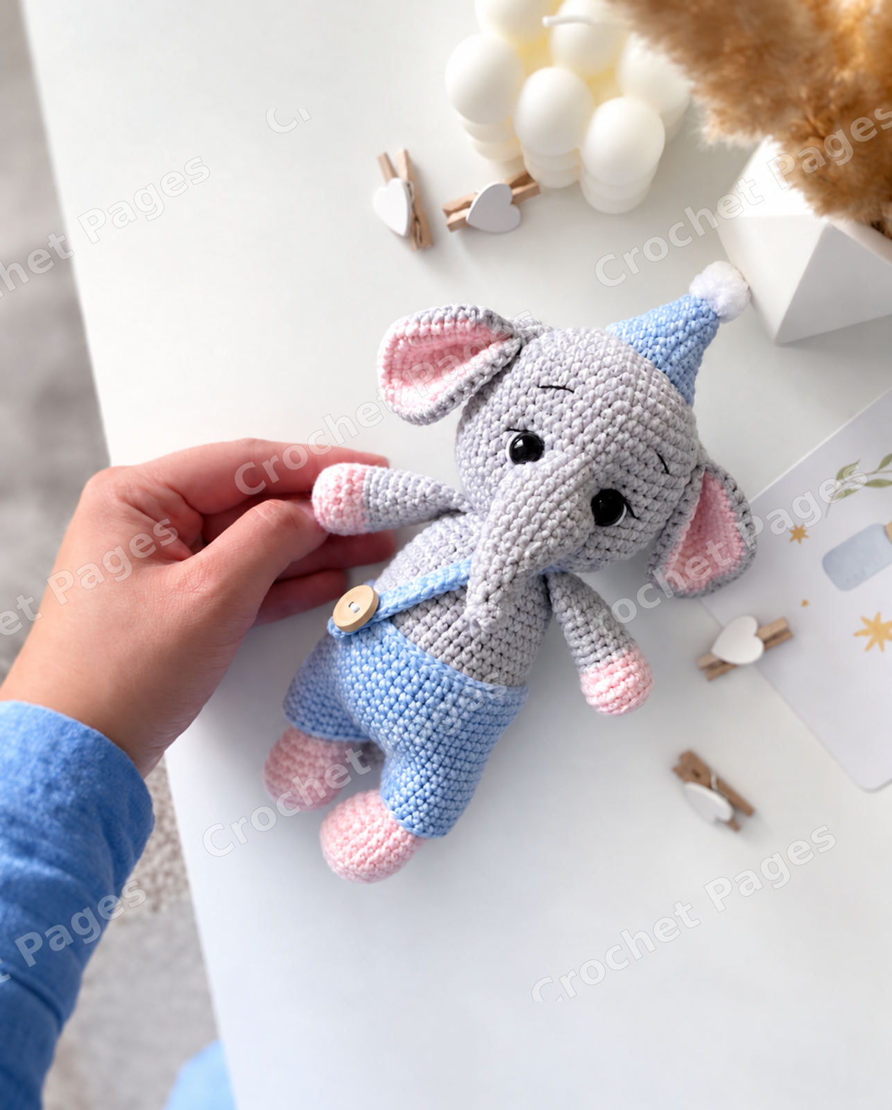 Crochet an elephant with a curved trunk, wide ears and contrasting paws, plus a crocheted cap and removable overalls. Finished-project view.